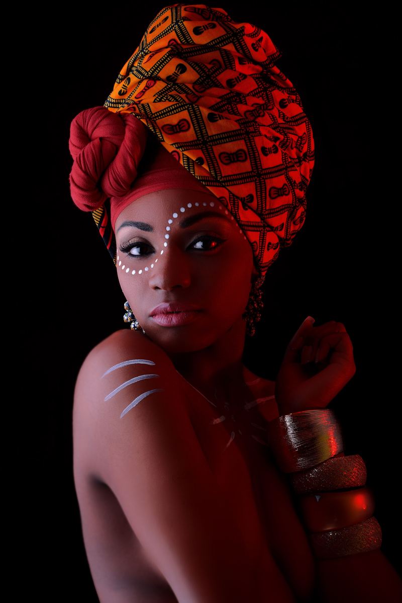 Portrait with an orange patterned headwrap and traditional white face dots