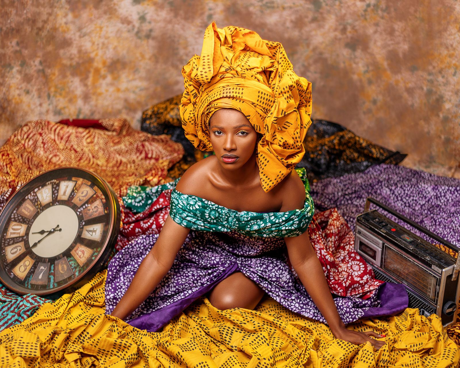 Eunice seated among vibrant African wax fabrics, wearing a golden headwrap